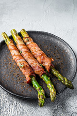 Plate with pork bacon wrapped asparagus on grey table. White background. Top view