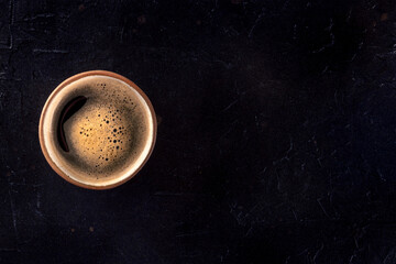 A cup of coffee with froth, overhead flat lay shot on a black background, with copy space