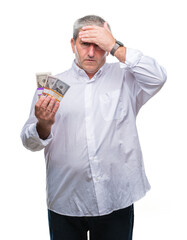 Handsome senior man holding bunch of money over isolated background stressed with hand on head, shocked with shame and surprise face, angry and frustrated. Fear and upset for mistake.