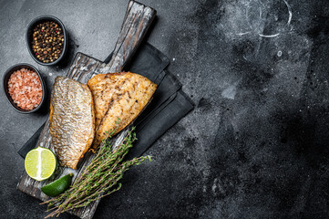 Roast Gilthead Sea Bream fillets with herbs on wooden board. Black background. Top view. Copy space