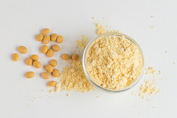 Soy flour in a glass bowl and soybeans scattered on a white background top view