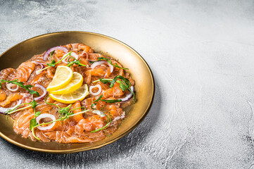 Fresh raw salmon carpaccio slices with onion and arugula served on a plate. White background. Top view. Copy space