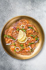 Fresh raw salmon carpaccio slices with onion and arugula served on a plate. White background. Top...