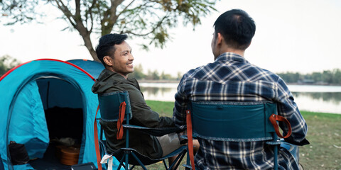 Gay LGBTQIA couple sitting on picnic chair drinking tea and coffee while camping on vacation holiday
