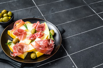 Prosciutto ham and melon salad in a plate. Black background. Top view. Copy space