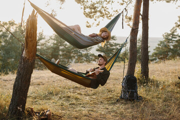 A guy and a girl are relaxing in hammocks in a pine forest at sunset. A couple in love rest in...