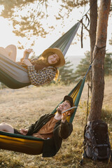 A guy and a girl are relaxing in hammocks in a pine forest at sunset.