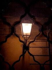 Un lampione acceso, di notte, visto attraverso la grata di una finestra.