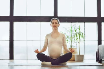 Fotobehang Meditation during pregnancy. Young calm tranquil pregnant woman doing yoga at home, meditating and practicing mindfulness, expectant mother sitting in lotus pose with closed eyes © Dasha Petrenko