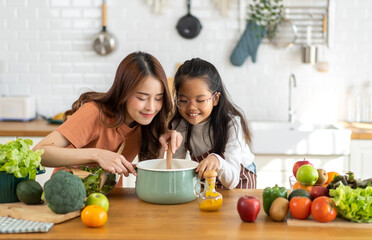 Portrait of enjoy happy love asian family mother with little asian girl daughter child help cooking food healthy eat with fresh vegetable testing smell soup in a pot with spoon.help mommy in kitchen
