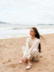 Fototapeta na wymiar Serene Beach Beauty: A Young Woman Enjoying the Sea Breeze in a Casual White Dress, Gazing at the Blue Ocean on a Sunny Summer Day