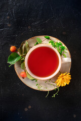 Tea with different ingredients. Teacup and herbs, fruits, and flowers, top shot on a black slate background. Healthy natural remedies