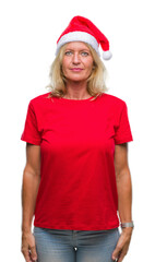 Middle age blonde woman wearing christmas hat over isolated background with serious expression on face. Simple and natural looking at the camera.