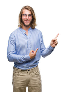 Young handsome man with long hair wearing glasses over isolated background with a big smile on face, pointing with hand and finger to the side looking at the camera.