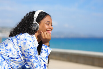Happy black woman listening online music on the beach