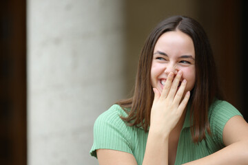 Happy woman laughing hiding mouth with hand in the street