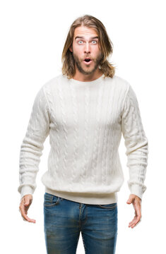 Young handsome man with long hair wearing winter sweater over isolated background afraid and shocked with surprise expression, fear and excited face.