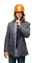 Young handsome architec man with long hair wearing safety helmet over isolated background asking to be quiet with finger on lips. Silence and secret concept.