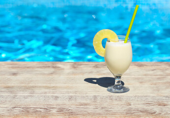 Glass of pinacolada cocktail standing on the swimming pool ledge