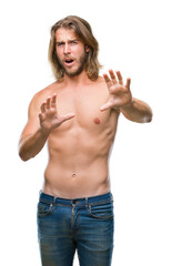 Young handsome shirtless man with long hair showing sexy body over isolated background afraid and terrified with fear expression stop gesture with hands, shouting in shock. Panic concept.