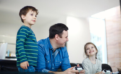 Smiling young man playing videogame together with son and daughter in modern living room