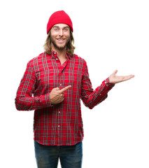 Young handsome man with long hair wearing red cap over isolated background amazed and smiling to the camera while presenting with hand and pointing with finger.