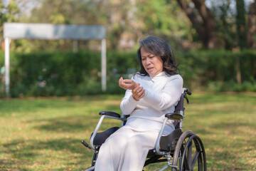 Asian elderly woman in wheelchair with arm pain in front yard.