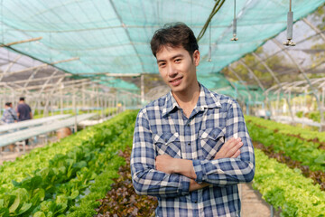 Asian man who owner a hydroponic garden stands with his arms crossed in the vegetable garden.