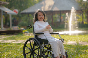 Happy old woman sitting in a wheelchair in park, healthy strong medical concept.