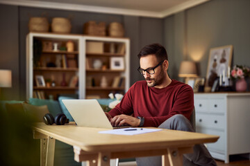 A young adult male freelance programmer deep in thought while typing on his laptop and working from...