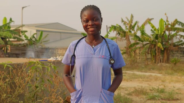 African female nurse doctor with stethoscope laughing smiling n front of camera in clinic hospital of Africa with palm tree village remote background 