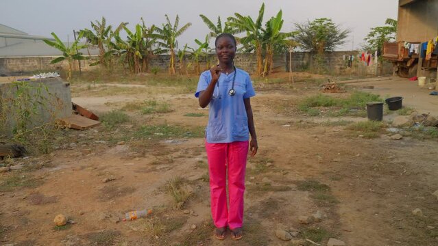 africa female doctor nurse with stethoscope saying I love you with hand gesture language sign In font of camera laughing in remote small village hospital clinic 