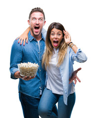 Young couple in love eating popcorn over isolated background very happy and excited, winner expression celebrating victory screaming with big smile and raised hands