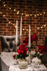 Luxurious decor for event with garland. Detail decor. Table decorated with tablecloth with flowers, candles. Romantic dinner by candlelight. Marriage proposal. Set up couple on evening Valentine's day - obrazy, fototapety, plakaty