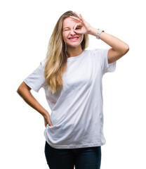 Obraz na płótnie Canvas Young beautiful blonde woman wearing casual white t-shirt over isolated background doing ok gesture with hand smiling, eye looking through fingers with happy face.