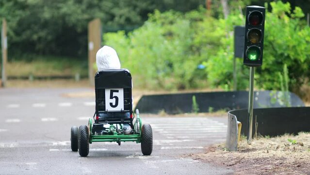 Preschooler girl driving pedal race car in amusement park with road surface marking and traffic lights