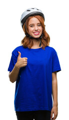 Young beautiful woman wearing cyclist helmet over isolated background doing happy thumbs up gesture with hand. Approving expression looking at the camera with showing success.