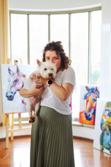 the artist with a white small dog East East Terrier examines her painting