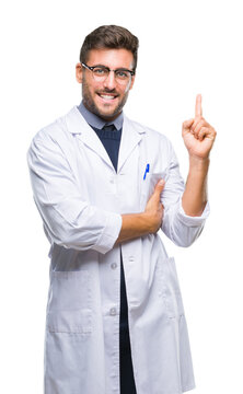Young handsome man wearing doctor, scientis coat over isolated background with a big smile on face, pointing with hand and finger to the side looking at the camera.