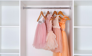 Assortment of children's dresses and skirts made of lush organza hangs in white wardrobe.