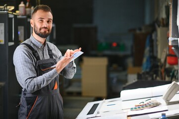 Print house worker controlling printing process quality and checking colors with magnifying glass