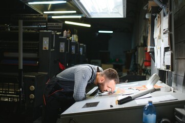Print house worker controlling printing process quality and checking colors with magnifying glass