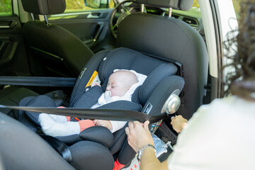 young mother adjusting the seat belt of her baby's transport seat in the car, child restraint system in the vehicle. safety concept in child transportation - obrazy, fototapety, plakaty