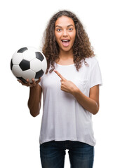 Young hispanic woman holding soccer football ball very happy pointing with hand and finger