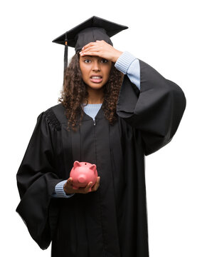 Young hispanic woman wearing graduation uniform holding piggy bank stressed with hand on head, shocked with shame and surprise face, angry and frustrated. Fear and upset for mistake.