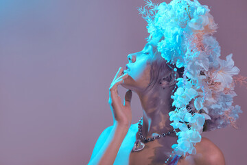 A sensual, gentle woman with a flower wreath on her head poses in blue lighting on a pink background