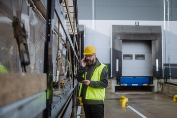 Warehouse receivers unloading of the truck in front of warehouse, phone calling checking delivered items.