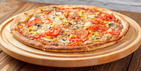 delicious pizza with chicken, mushrooms, cheese, tomatoes and corn on a wooden background