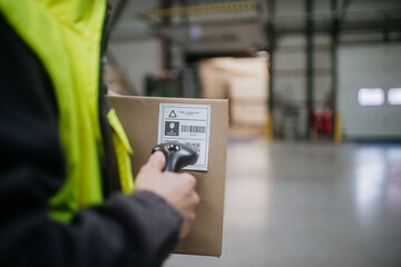 Warehouse worker scanning barcode on cardboard box. Receiving clerk holding scanner checking delivered goods against order.