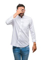Adult hispanic man over isolated background peeking in shock covering face and eyes with hand,...